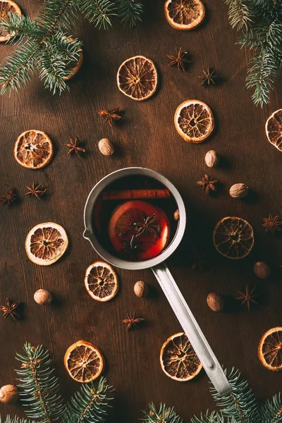 Vista superior del vino caliente condimentado en cacerola con rodajas de naranja secas sobre fondo de madera con ramas de pino - foto de stock