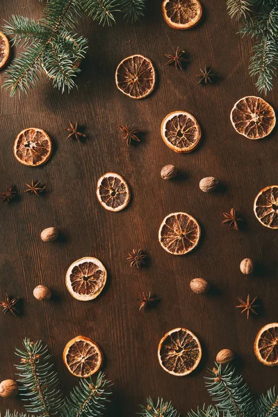 Vue de dessus des tranches d'orange séchées, des étoiles d'anis et des graines de noix de muscade sur fond de bois avec des branches de sapin — Photo de stock