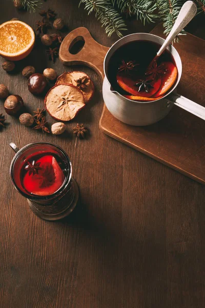 Hot mulled wine in saucepan and glass cup with spices on wooden background — Stock Photo