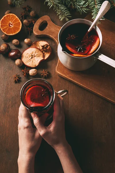 Cropped view of woman holding glass of mulled wine on wooden background — Stock Photo