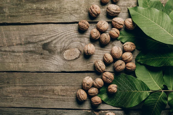 Top view of whole natural walnuts and green leaves on wooden table — Stock Photo