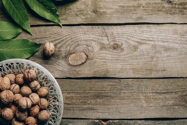 Вид зверху смачні здорові волоські горіхи на тарілці і зелене листя на дерев'яному столі — стокове фото