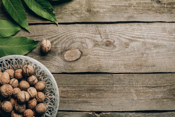 Vista superior de las sabrosas nueces sanas en el plato y hojas verdes en la mesa de madera - foto de stock