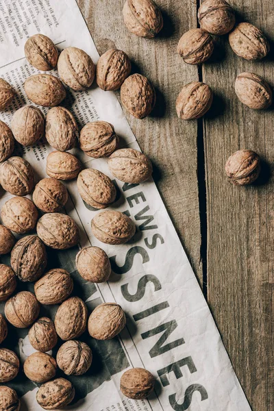 Top view of whole walnuts and business newspaper on wooden table — Stock Photo