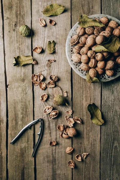 Top view of whole walnuts on plate, nutshells and nutcracker on wooden table — Stock Photo