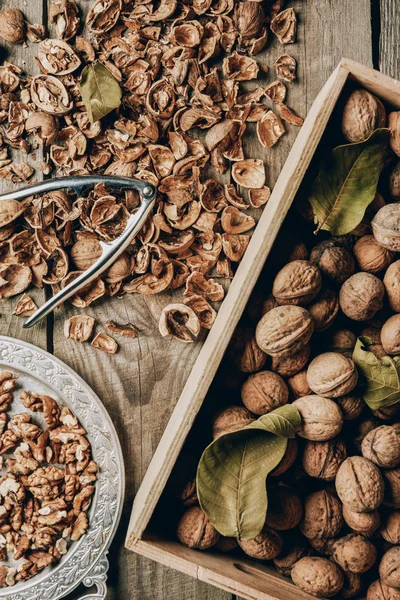 Top view of walnuts in box, nutcracker and nutshells on wooden table — Stock Photo