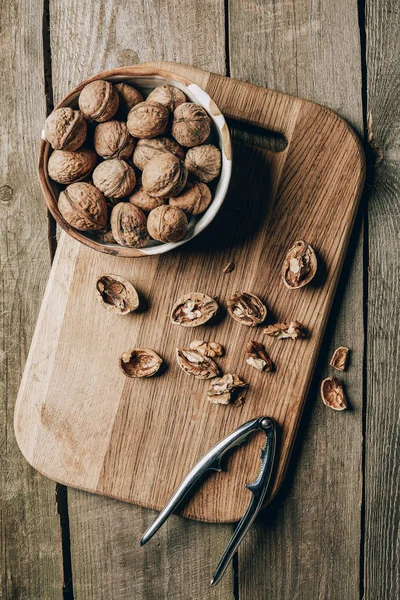 Top view of walnuts in bowl and nutcracker on chopping board on wooden table — Stock Photo