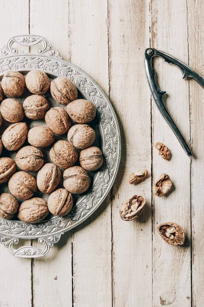 Top view of walnuts on vintage plate and nutcracker on wooden table — Stock Photo