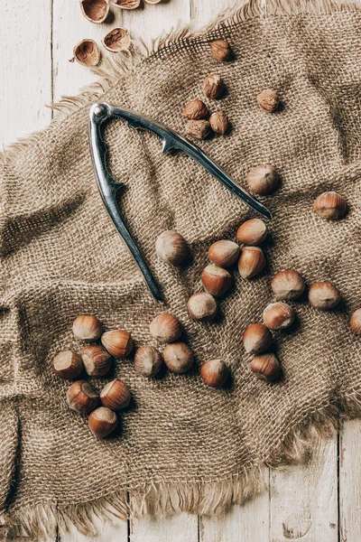 Top view of tasty hazelnuts and nutcracker on sackcloth on wooden table — Stock Photo