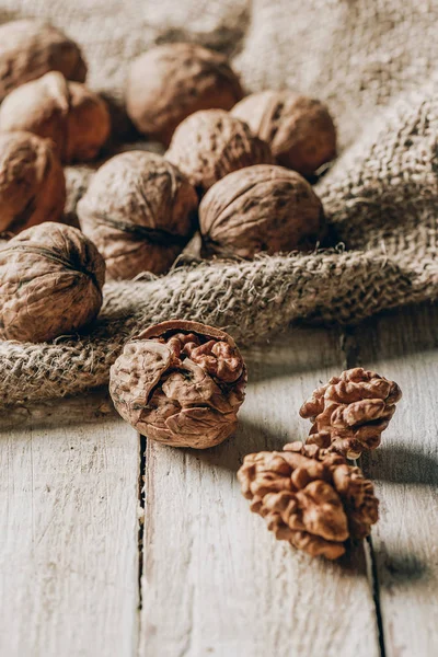 Close-up view of whole and cracked walnuts and sackcloth on wooden table — Stock Photo