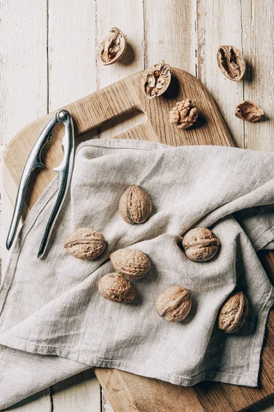 Top view of walnuts on cloth, chopping board and nutcracker on wooden table — Stock Photo