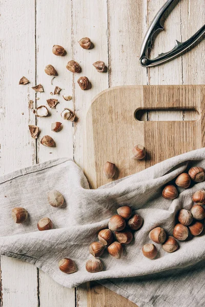 Vue du dessus des noisettes sur tissu, planche à découper et casse-noisettes sur table en bois — Photo de stock