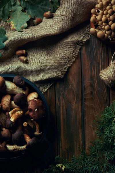 Top view of fresh picked edible mushrooms in pan and bowl, sackcloth and rope on wooden table — Stock Photo