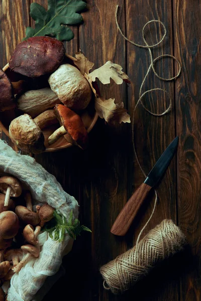 Top view of fresh picked delicious mushrooms, knife and rope on wooden table — Stock Photo