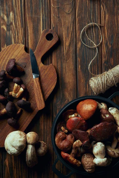 Top view of fresh raw mushrooms, chopping board, knife, pan and rope on wooden table — Stock Photo