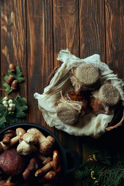 Vista superior de deliciosos cogumelos em conserva na cesta e cogumelos frescos na panela na mesa de madeira — Fotografia de Stock
