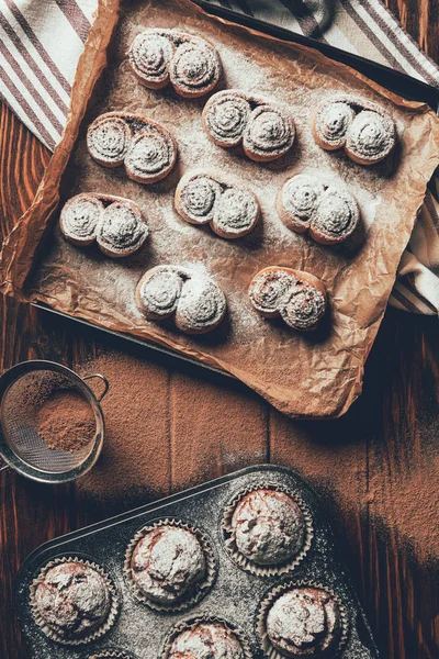 Vista superior de biscoitos cozidos no forno saborosos e muffins com açúcar em pó em bandejas na padaria — Fotografia de Stock