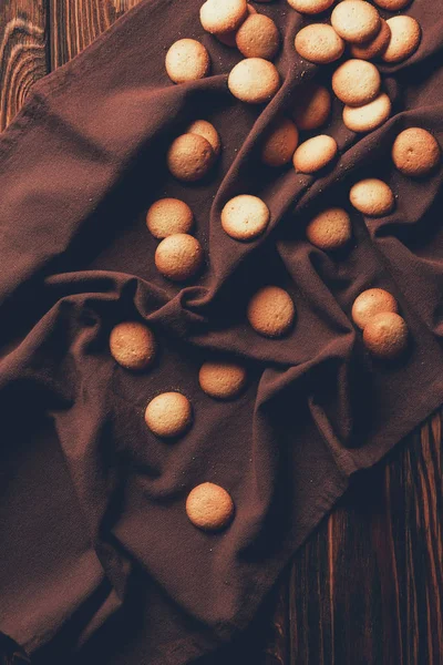 Top view of tasty baked cookies scattered on tablecloth on wooden table in bakery — Stock Photo