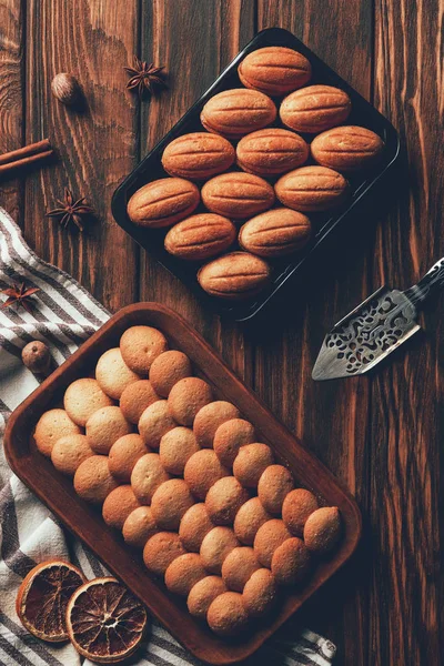 Blick von oben auf leckere hausgemachte gebackene Plätzchen auf Blechen auf Holztisch in Bäckerei — Stockfoto