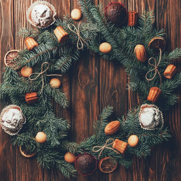 Tannenkranz mit leckeren gebackenen Plätzchen und Muffins auf Holztisch, Weihnachtskonzept — Stockfoto