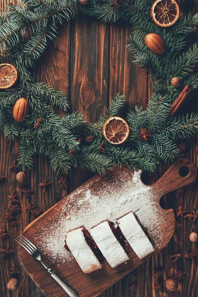 Blick von oben auf leckeres Gebäck auf Schneidebrett und Tannenkranz auf Tisch, Weihnachtskonzept — Stockfoto