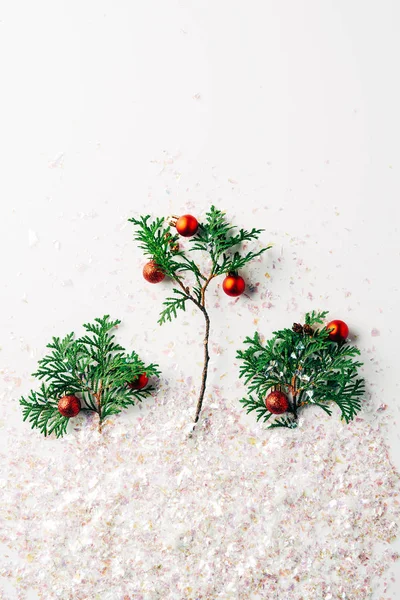 Flat lay with pine tree branches decorated with christmas balls with glitters on white surface — Stock Photo