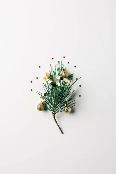 Vista superior de la pequeña rama de pino con cinta y bolas de Navidad en la superficie blanca - foto de stock