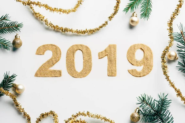 Вид зверху на знак 2019 року, соснові гілки, золоті гірлянди та різдвяні кульки на білому тлі — стокове фото