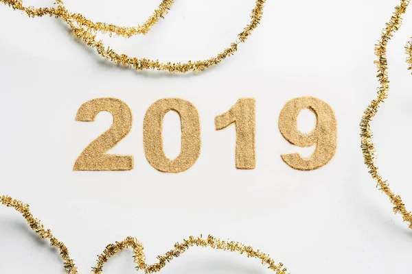 Vue du dessus de 2019 année signe fait de paillettes dorées et guirlandes sur fond blanc — Photo de stock