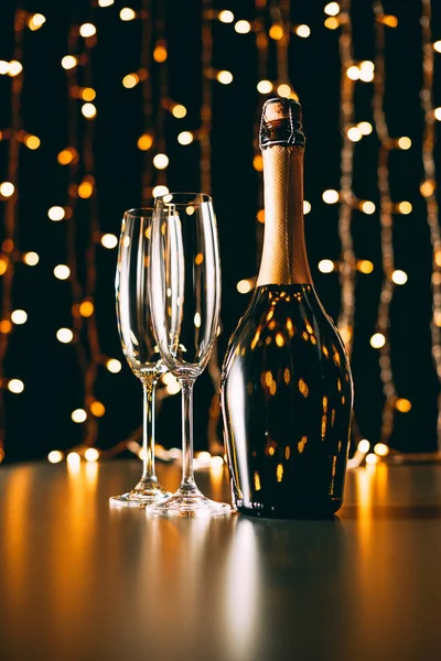 Champagne bottle and glasses on garland light background, christmas concept — Stock Photo