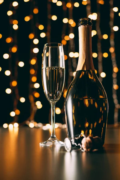 Copa de champán y botella sobre fondo claro guirnalda, concepto de Navidad - foto de stock