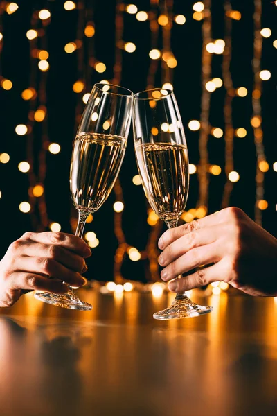 Cropped image of couple clinking with glasses of champagne on garland light background, christmas concept — Stock Photo