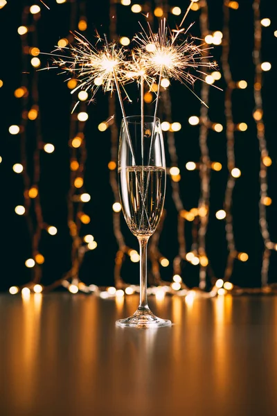 Champán con destellos de Navidad sobre fondo claro guirnalda - foto de stock