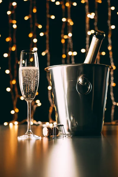 Botella de champán en cubo y vidrio sobre fondo claro guirnalda, concepto de Navidad - foto de stock