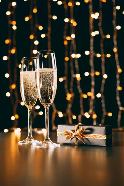 Copas de champán y presentes sobre fondo claro guirnalda, concepto de Navidad - foto de stock