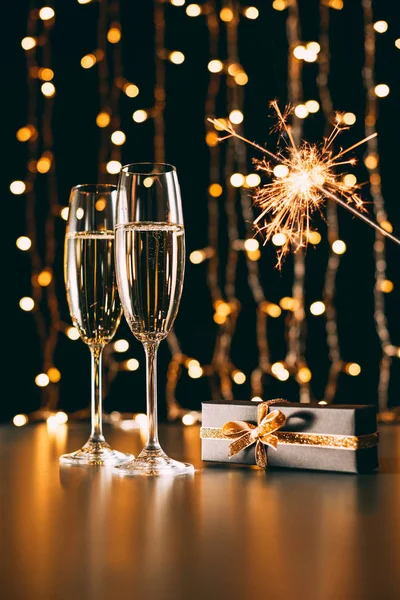 Glasses of champagne, present and christmas sparkle on garland light background, christmas concept — Stock Photo