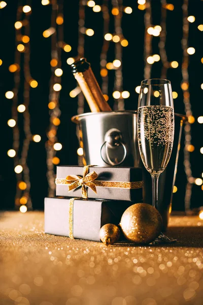 Champagne in bucket and presents on garland light background, christmas concept — Stock Photo