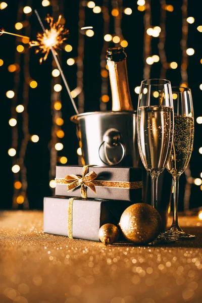 Champán en cubo, regalos y brillo de Navidad sobre fondo claro guirnalda - foto de stock