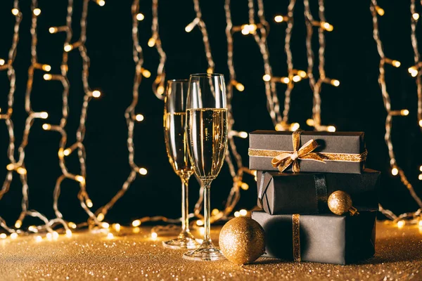 Weihnachtsgeschenke und Sektgläser auf hellem Girlanden-Hintergrund — Stockfoto