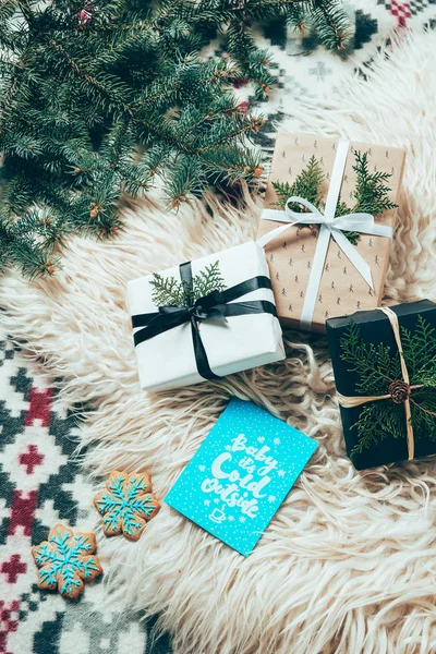 Flache Lage mit Tannenzweigen, Plätzchen, Winterpostkarten und verpackten Weihnachtsgeschenken auf wollenen Hintergrund — Stockfoto