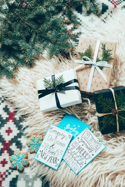 Flache Lage mit Tannenzweigen, Plätzchen, Winterpostkarten und verpackten Weihnachtsgeschenken auf wollenen Hintergrund — Stockfoto