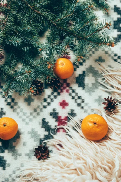 Top view of pine tree branches, pine cones and fresh tangerines on blanket backdrop — Stock Photo