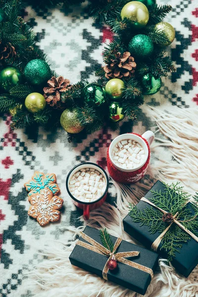 Draufsicht auf Tassen mit Heißgetränken mit Marshmallows, Plätzchen, Adventskranz und Geschenken auf Deckenhintergrund, weihnachtliches Frühstückskonzept — Stockfoto