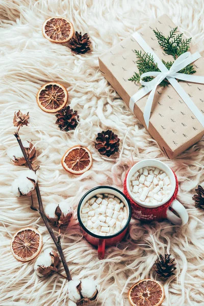 Flat lay with cup of cocoa with marshmallows, wrapped christmas present and cotton twig on woolen background — Stock Photo