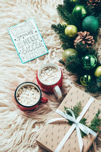 Top view of christmas wreath, cups of cocoa drinks with marshmallows and postcard with have yourself marry little christmas lettering on woolen backdrop — Stock Photo