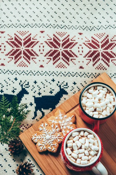 Vista superior de xícaras de chocolate quente com marshmallows e biscoitos no fundo do suéter, conceito de café da manhã de Natal — Fotografia de Stock