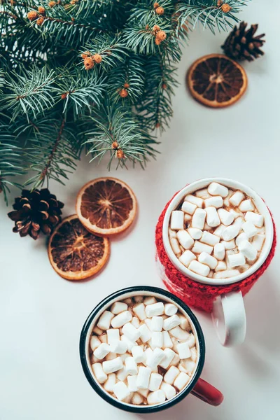 Draufsicht auf Tassen mit heißer Schokolade mit Marshmallows und Tannenzweigen auf weißer Oberfläche, Weihnachtsfrühstückskonzept — Stockfoto