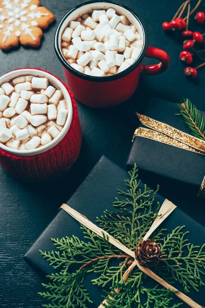 Top view of wrapped christmas presents and cups of hot chocolate with marshmallows on black tabletop — Stock Photo