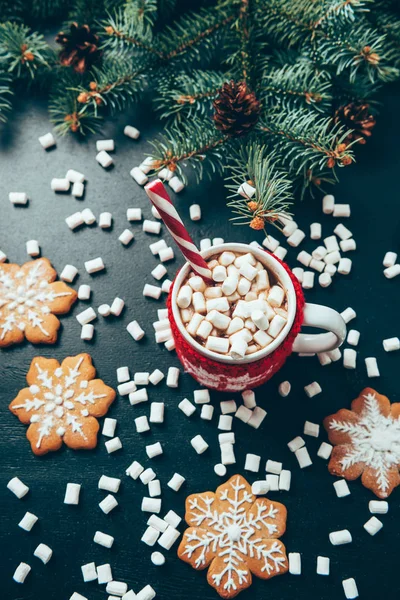 Posa piatta con tazza di bevanda calda con marshmallow, biscotti e rami di pino su tavolo nero, Natale e Capodanno concetto di vacanze — Foto stock