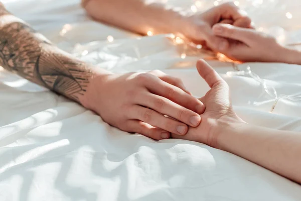 Partial view of couple holding hands while lying in bed with garland — Stock Photo